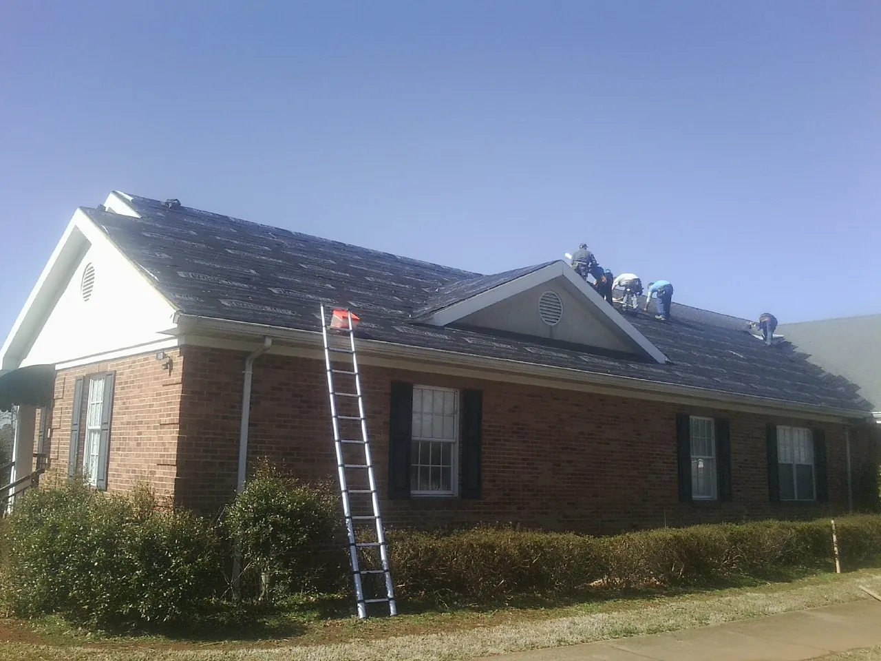 Crew tearing shingles off a brick ranch roof with a ladder set — Metal Roof Repair work by our crew in Farmingdale