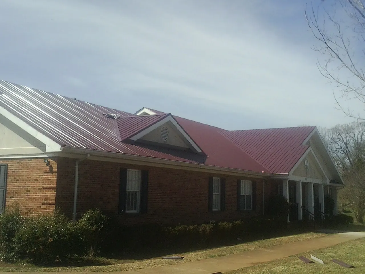 Red metal roof with gabled entries on a long brick building, from a Hail Damage Roof Repair job in Farmingdale