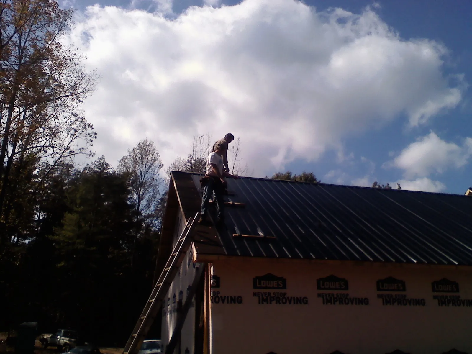 Roofer fastening dark metal panels high against a cloudy sky, from a Roof Inspection job in Farmingdale