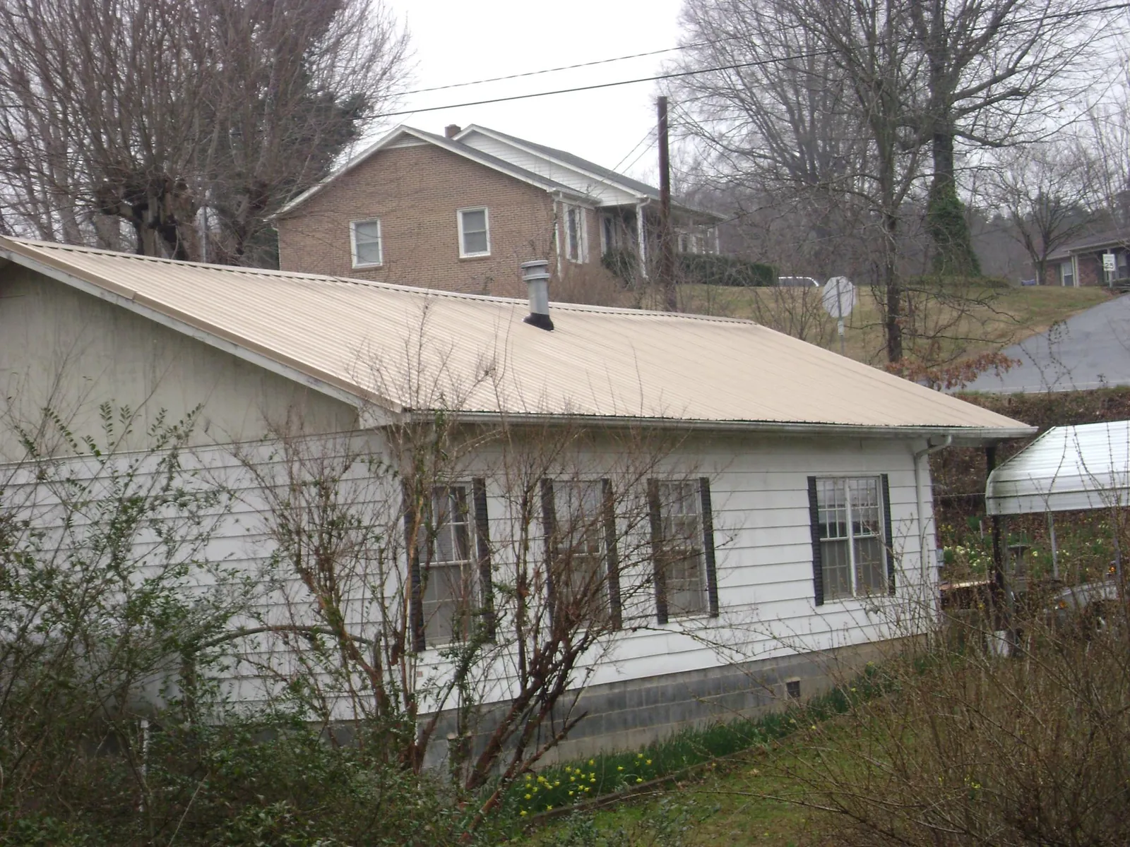 Tan metal roof on a white sided house set into a hillside — Commercial Roofing by Roofing Brothers in Farmingdale