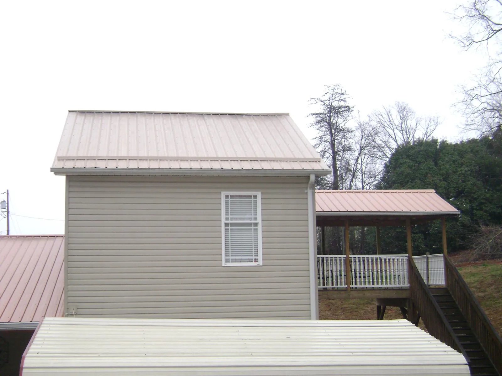 Tan metal roofs on a two story addition and attached porch, from a Roof Replacement job in Farmingdale